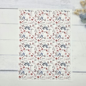 May include: A rectangular sheet featuring a repeating pattern of white ghosts interspersed with dark blue foliage and small red flowers. The design is arranged in a dense, uniform grid across the entire surface of the white paper material.