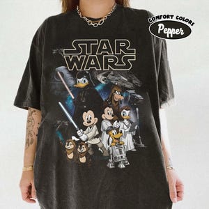 May include: Black t-shirt with a Star Wars graphic featuring Disney characters. The design includes Darth Vader as Donald Duck, Mickey Mouse, and other characters in Star Wars attire. The shirt has a Comfort Colors Pepper label.