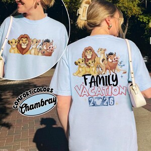 以下が含まれることがあります： ライオンのキャラクターのグラフィックと「Family Vacation 2026」の文字が入った水色のTシャツ。シャツはComfort Colors Chambray生地で作られています。