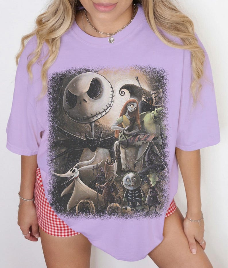 May include: A light purple short-sleeve t-shirt featuring a large, detailed graphic print of characters from The Nightmare Before Christmas, including Jack Skellington, Sally, Zero, and the trick-or-treaters, set against a dark, textured background.
