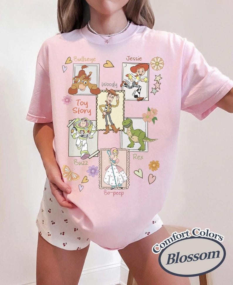 Puede incluir: Camiseta rosa claro con un dise&ntilde;o gr&aacute;fico de personajes de la pel&iacute;cula "Toy Story", incluyendo a Woody, Buzz Lightyear, Jessie, Rex, Bullseye y Bo-Peep. El dise&ntilde;o tambi&eacute;n incluye el texto "Toy Story" y "Comfort Colors Blossom".