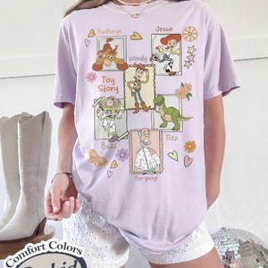 Puede incluir: Una camiseta de color lila claro con ilustraciones de personajes de la pel&iacute;cula "Toy Story". El dise&ntilde;o incluye a Bullseye, Woody, Buzz, Rex, Jessie y Bo-Peep. Las palabras "Toy Story" est&aacute;n impresas en la camiseta.