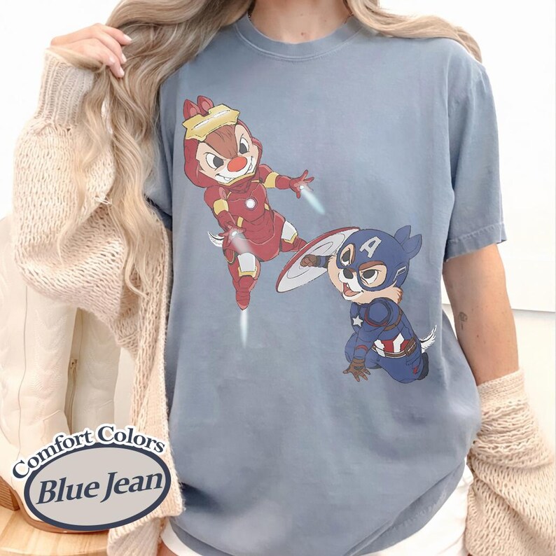 May include: Blue jean colored t-shirt featuring cartoon characters dressed as superheroes. One character is in a red Iron Man suit, and the other is in a Captain America suit. The shirt has the words "Comfort Colors Blue Jean" printed on it.