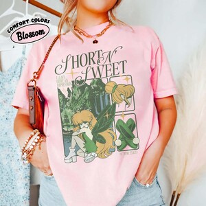 Puede incluir: Camiseta rosa claro con la frase "Short N Sweet" y un gr&aacute;fico de hada. El dise&ntilde;o incluye una escena de bosque, una ilustraci&oacute;n de hada y zapatos verdes. Tambi&eacute;n incluye el texto "Leave Quite An Impression". La camiseta est&aacute; etiquetada como "Comfort Colors Blossom".