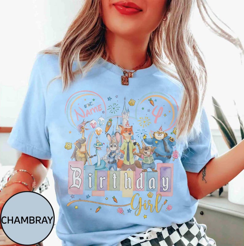 以下が含まれることがあります： 水色のTシャツ。映画「ズートピア」のキャラクター、お城、そして「Birthday Girl」の文字がカラフルに描かれています。デザインには名前と数字の「4」を入れられるスペースがあります。Tシャツは丸首で半袖です。