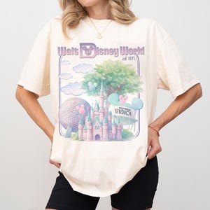 Puede incluir: Camiseta color crema con un gr&aacute;fico de Walt Disney World est. 1971. El dise&ntilde;o incluye un castillo, Spaceship Earth, nubes y orejas de Mickey Mouse en colores pastel. La camiseta es de corte holgado.