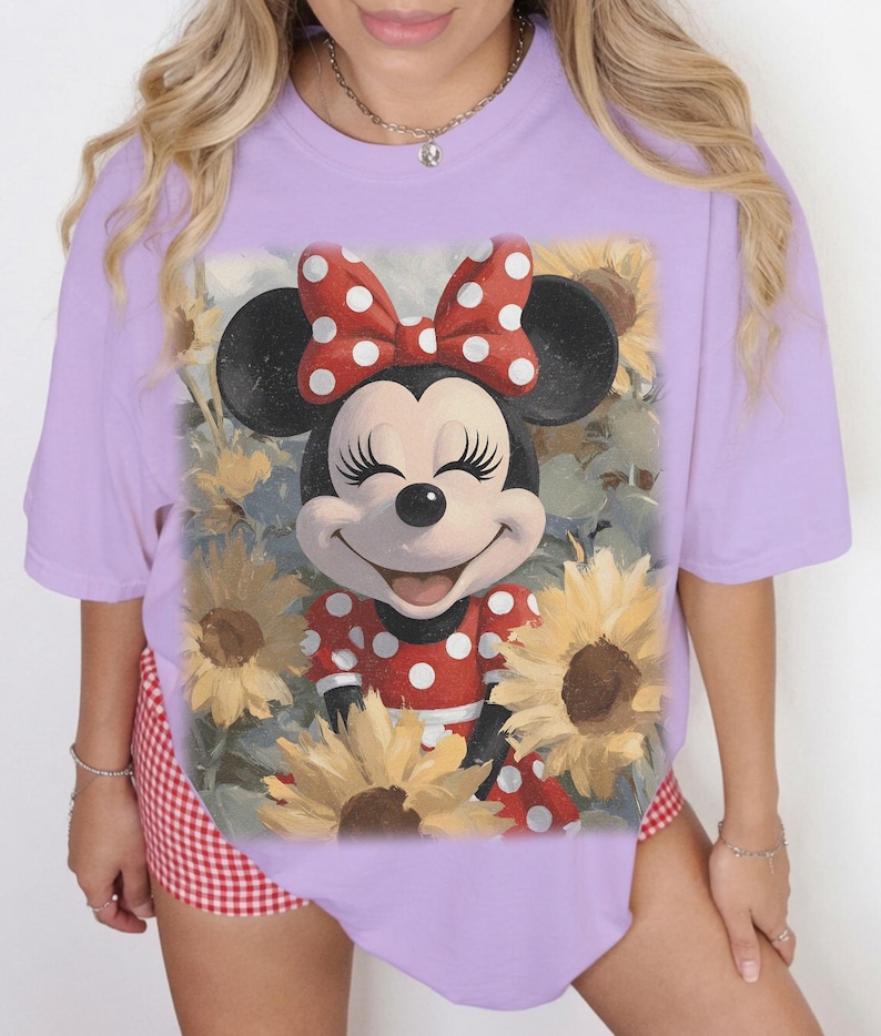 Puede incluir: Una camiseta de manga corta de color morado claro con un estampado gr&aacute;fico de Minnie Mouse con un vestido y un lazo de lunares rojos y blancos, rodeada de girasoles amarillos. El personaje tiene orejas negras y una expresi&oacute;n sonriente.