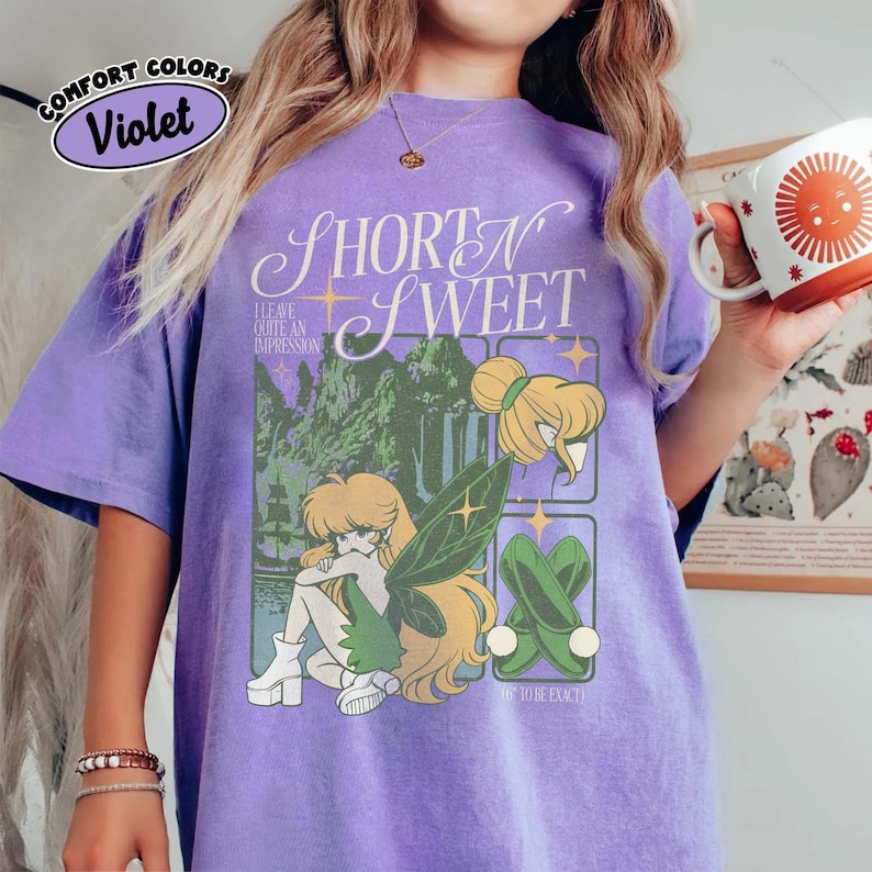 Puede incluir: Camiseta violeta Comfort Colors con la frase "Short N Sweet" y un dise&ntilde;o de hada. El dise&ntilde;o incluye un hada con alas verdes, un paisaje forestal y el texto "I leave quite an impression".