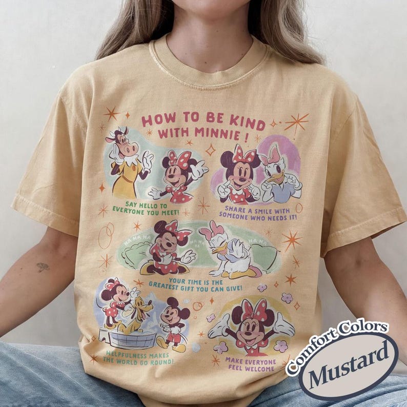 Puede incluir: Camiseta de color mostaza con Minnie Mouse y sus amigos, con el texto "HOW TO BE KIND WITH MINNIE!". La camiseta tiene un dise&ntilde;o vintage con varias ilustraciones y frases. Es una camiseta de la marca Comfort Colors.