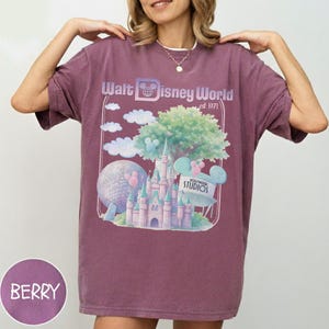 Puede incluir: Camiseta color bayas con un gr&aacute;fico de Walt Disney World, est. 1971. El dise&ntilde;o incluye un castillo, Spaceship Earth, nubes y el logotipo de Hollywood Studios. La camiseta tiene mangas cortas y cuello redondo.