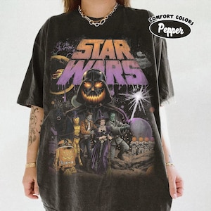 May include: A pepper-coloured t-shirt featuring a graphic print with the text Star Wars. The design depicts Darth Vader as a jack-o'-lantern, alongside various characters dressed in Halloween costumes, including a droid and a witch, on a dark background.
