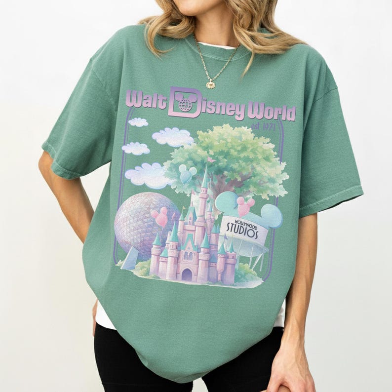 Puede incluir: Camiseta verde con un dise&ntilde;o de Walt Disney World. El dise&ntilde;o incluye un castillo, Spaceship Earth, nubes y el texto "Walt Disney World Est. 1971" y "Hollywood Studios". La camiseta tiene mangas cortas y un corte holgado.