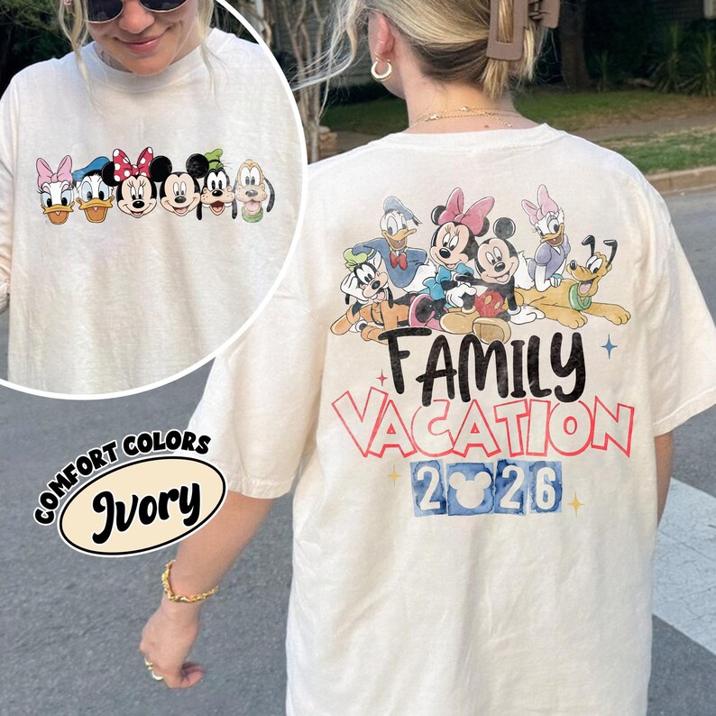 以下が含まれることがあります： ミッキーマウスとミニーマウス、ドナルドダックとデイジーダック、グーフィーとプルートを含むディズニーキャラクターのグラフィックが特徴の、アイボリー色の長袖Tシャツ。「Family Vacation 2026」の文字が背面に表示されています。