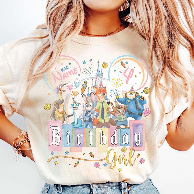 以下が含まれることがあります： クリーム色のTシャツ。カラフルな漫画のキャラクター、お城、そして「Birthday Girl」の文字が描かれています。デザインには数字の「4」と名前を入れるスペースがあり、星と花のアクセントが施されています。