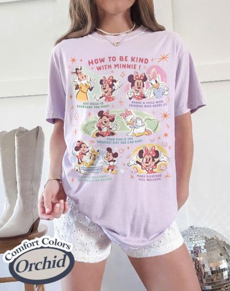 Puede incluir: Una camiseta lila Comfort Colors con un gr&aacute;fico de Minnie Mouse y sus amigos. La camiseta tiene el texto "HOW TO BE KIND WITH MINNIE!" y otras frases. La camiseta se combina con pantalones cortos blancos.