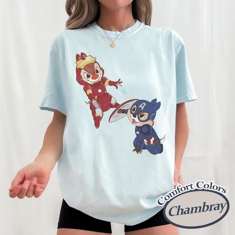 May include: Light blue t-shirt featuring cartoon characters Chip and Dale dressed as Iron Man and Captain America. The shirt has the words "Comfort Colors Chambray" printed on the bottom right corner. The shirt is a light blue color.
