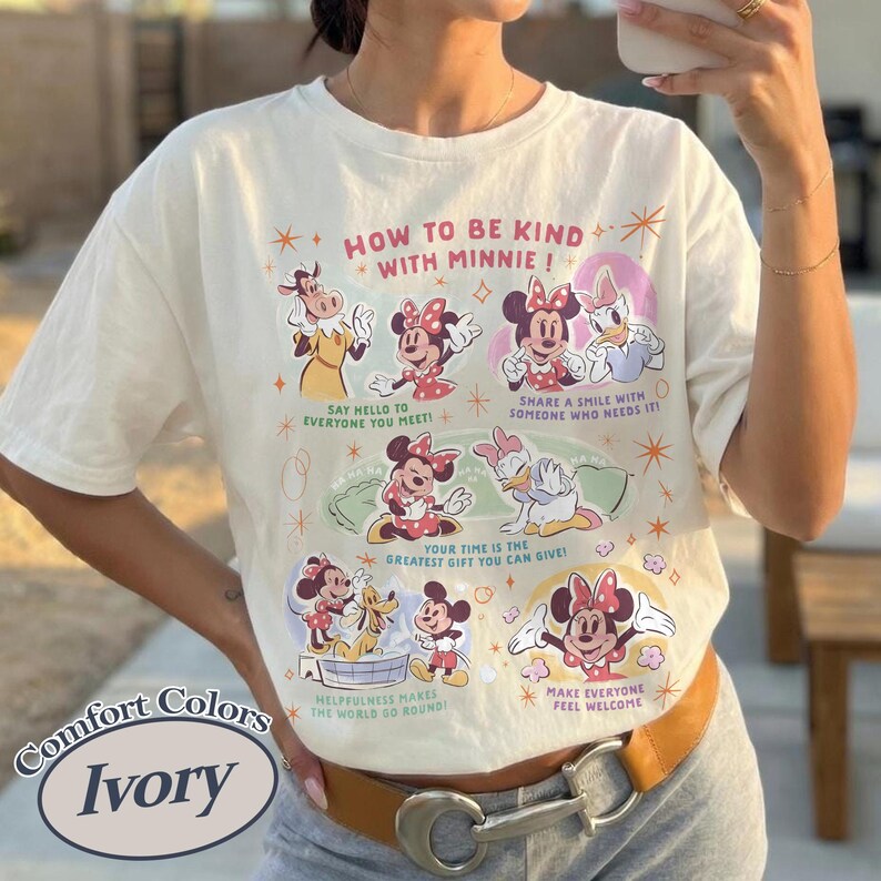 Puede incluir: Camiseta de color marfil con un dise&ntilde;o de Minnie Mouse y sus amigos, con el texto "How to be kind with Minnie!". El dise&ntilde;o incluye varios personajes y frases. La camiseta tiene un corte holgado y est&aacute; hecha de un material suave.