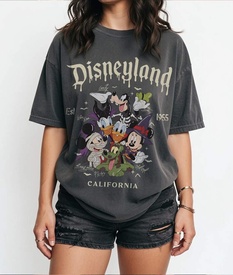 May include: A charcoal gray short-sleeve t-shirt featuring the text Disneyland Est 1955 California. The graphic displays cartoon characters including Mickey Mouse, Minnie Mouse, Donald Duck, Daisy Duck, Goofy, and Pluto in Halloween costumes.