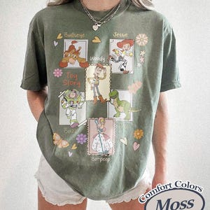Puede incluir: Camiseta verde oliva con ilustraciones de personajes de dibujos animados de la pel&iacute;cula Toy Story. La camiseta incluye a Woody, Buzz Lightyear, Jessie, Bo Peep, Bullseye y Rex. Tambi&eacute;n tiene las palabras "Toy Story" y "Comfort Colors Moss".