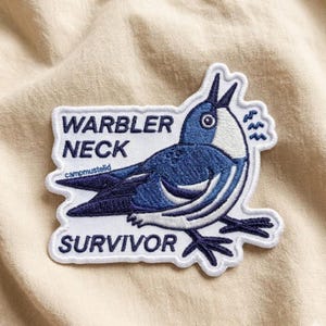 May include: Embroidered patch featuring a blue and white bird with the text "WARBLER NECK SURVIVOR." The patch has a white border and is set against a beige fabric background. The patch includes the text "campmustelid."
