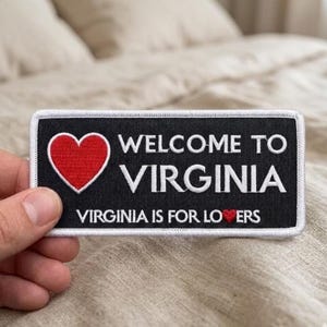 May include: A rectangular patch with a black background and white border. The patch features a red heart and the words "WELCOME TO VIRGINIA" and "VIRGINIA IS FOR LOVERS" in white text.