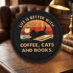 May include: Round black patch with the text "LIFE IS BETTER WITH COFFEE, CATS AND BOOKS." The patch features a cat silhouette, a coffee cup, and an open book against a sunset background. The patch is on a wooden surface.
