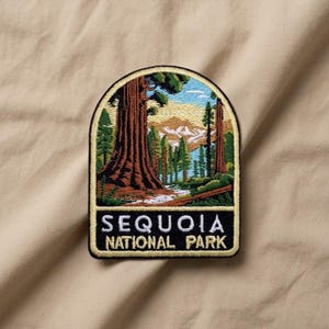 May include: Embroidered patch featuring a scenic view of Sequoia National Park. The patch depicts a large redwood tree, a river, and mountains under a blue sky. The text "SEQUOIA NATIONAL PARK" is displayed in white letters on a black background.