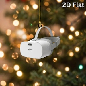 May include: A white virtual reality headset ornament with a gray head strap and the text 2D Flat printed in the upper right corner. The device features a central black sensor and a small logo on the front, suspended by a thin gold string.