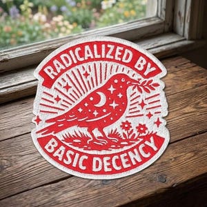 May include: Embroidered patch with the text "RADICALIZED BY BASIC DECENCY" in a red, arched banner. The patch features a red bird with a crescent moon and stars, holding a sprig. The design includes radiating lines and floral elements.