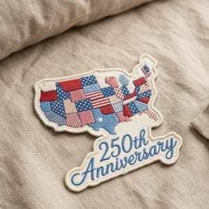 May include: Embroidered patch in the shape of the United States, featuring a patchwork design in red, white, and blue. The patch reads "250th Anniversary" in blue script, celebrating a milestone.