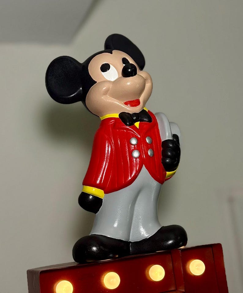 Peut inclure: Figurine de Mickey Mouse en veste rouge, pantalon gris et chaussures noires. La figurine a des oreilles noires, un visage bronz&eacute; et un sourire rouge. Il tient un objet gris et se tient sur une base rouge avec des lumi&egrave;res. Un objet de collection Disney classique.