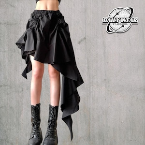 Könnte beinhalten: Schwarzer asymmetrischer Rock mit Rüschendesign und langem, fließendem Panel. Der Rock hat einen elastischen Bund und wird mit schwarzen Schnürstiefeln getragen. Das Bild enthält den Text "DAILY WEAR BY JEANINA" in einem kreisförmigen Logo.