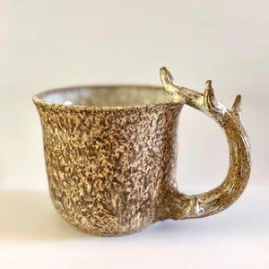 May include: A set of three ceramic mugs with a speckled, matte finish. The mugs are in shades of cream, light gray, and dark gray. Each mug has a simple, minimalist design, perfect for coffee or tea.