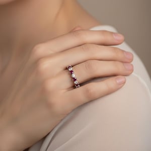 Op de afbeelding: Een zilveren ring met afwisselend rode en heldere edelstenen. De ring wordt aan een vinger gedragen. De ronde edelstenen zijn dicht op elkaar geplaatst, waardoor een doorlopend patroon rond de band ontstaat.