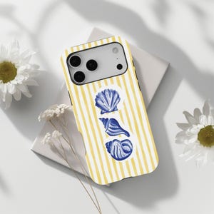 Könnte beinhalten: Eine Handyhülle mit gelb-weißem Streifenmuster und drei blauen Muscheldarstellungen. Die Hülle liegt auf einer weißen Oberfläche, mit weißen Blumen im Hintergrund.