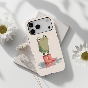 Puede incluir: Funda de teléfono con un dibujo de una rana con botas de agua rosas, de pie en un charco bajo una lluvia ligera. La funda tiene un fondo crema y un borde negro. La rana tiene una expresión triste.