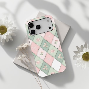 May include: A phone case with a pastel floral design. The case features a repeating pattern of pink, green, and white squares, each adorned with teacups, bows, and floral motifs. The case is designed to fit a smartphone.