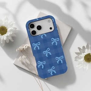 Pode incluir: Uma capa retangular para smartphone com um padrão xadrez em azul escuro e azul médio, decorada com ícones repetidos de laços de fita azul claro. A capa tem um recorte para um sistema de câmara de três lentes no canto superior esquerdo.