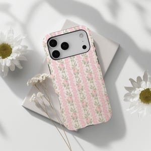 Pode incluir: Uma capa de smartphone com um padrão repetitivo de listras verticais cor-de-rosa e delicadas vinhas florais com pequenas rosas cor-de-rosa e folhas verdes sobre um fundo creme. A capa tem uma área de câmara preta com três lentes.