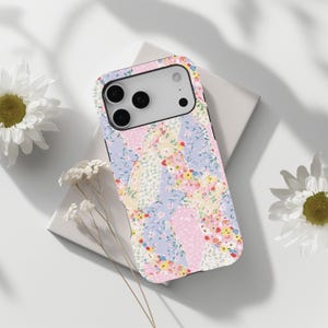 Puede incluir: Una funda de teléfono con un diseño de patchwork floral en tonos pastel. La funda tiene un borde negro y un recorte para la cámara. El diseño incorpora patrones florales rosas, azules, amarillos y blancos.