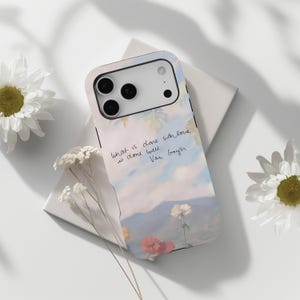 May include: A phone case featuring a pastel landscape design with flowers and a quote by Van Gogh. The case has a soft color palette of blues, pinks, and greens, with the quote "What is done with love is done well." The case is shown with white flowers.