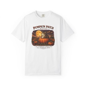 May include: A white t-shirt featuring a graphic of a cat sitting on a pumpkin in a patch under a full moon. The text reads PUMPKIN PATCH SUPERVISOR, ALL PUMPKINS INSPECTED, ALL PUMPKINS MINE. The illustration uses warm orange, brown, and purple tones.