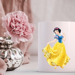 May include: A white ceramic mug featuring a colorful illustration of Snow White in her iconic blue and yellow dress. The mug is set next to a pink carnation flower in a silver vase.