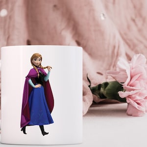 May include: White ceramic mug featuring a full-color image of a cartoon character in a blue dress, purple cape, and black boots. The character has blonde braids and is holding her hair. A pink flower and fabric are in the background.