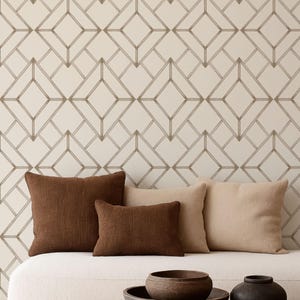 May include: A living room scene featuring a white sofa with four throw pillows in shades of brown and beige. A dark brown coffee table holds two dark brown bowls and a black vase. The wall has a geometric pattern.