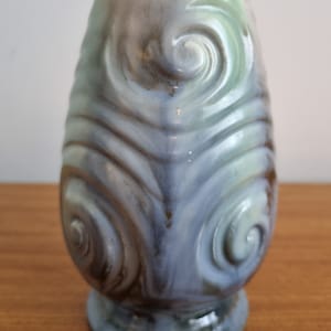 May include: A ceramic vase with a light blue, green, and brown glaze. The vase has a swirling pattern and a rounded base.