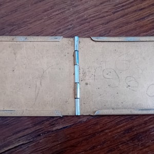 May include: A small, brown, rectangular, hinged photo album with a silver metal frame. The album is closed and has the word "Fred" written on the right side.
