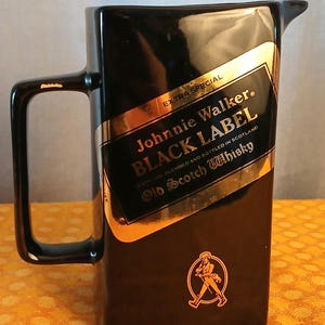 May include: Black ceramic pitcher with a handle and a spout. The pitcher features a gold and black label with the text "Johnnie Walker BLACK LABEL Old Scotch Whisky". A gold emblem of a man walking is on the bottom.