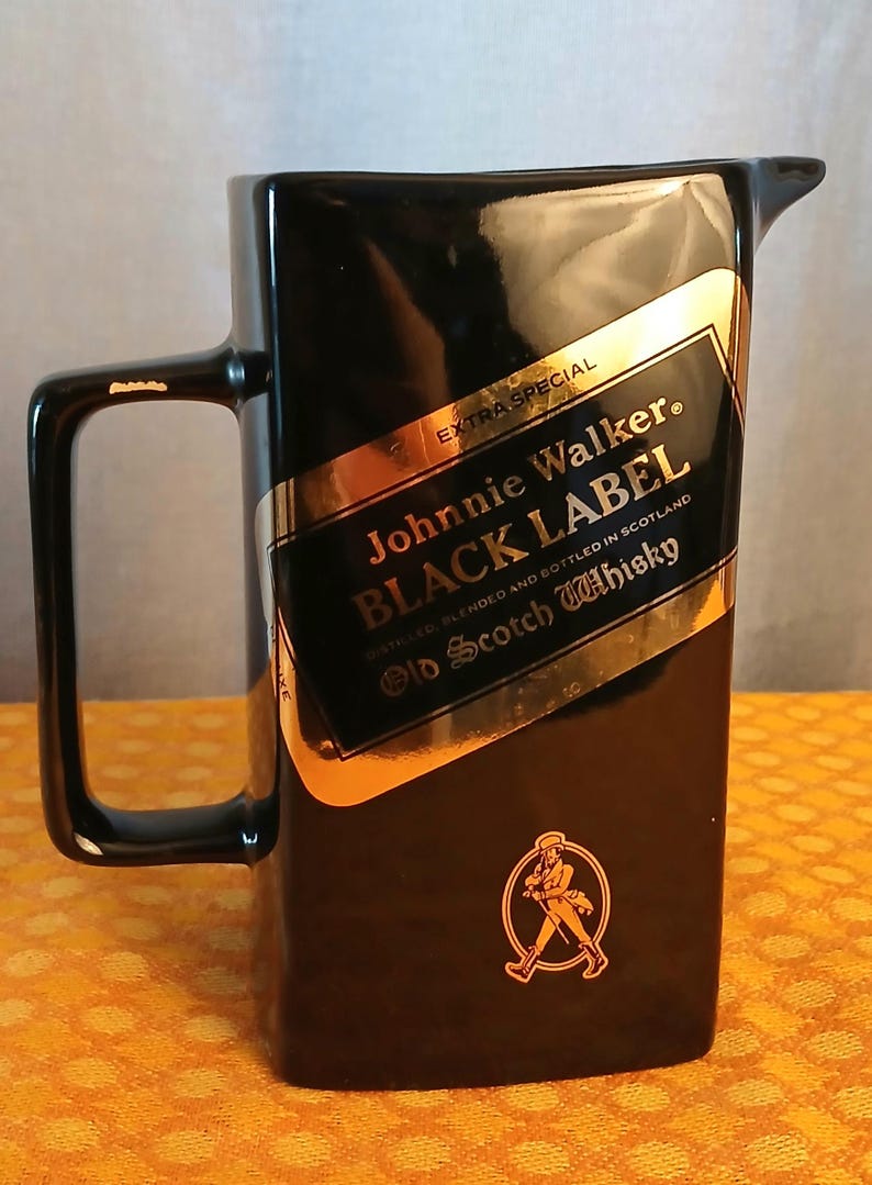 May include: Black ceramic pitcher with a handle and a spout. The pitcher features a gold and black label with the text "Johnnie Walker BLACK LABEL Old Scotch Whisky". A gold emblem of a man walking is on the bottom.