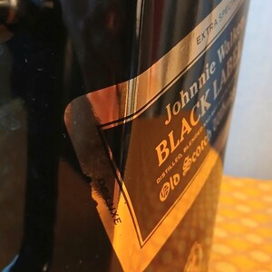 May include: Black ice bucket with a gold and black label that reads "Johnnie Walker BLACK LABEL". The label also says "Extra Special" and "Deluxe". The bucket is on a yellow surface.